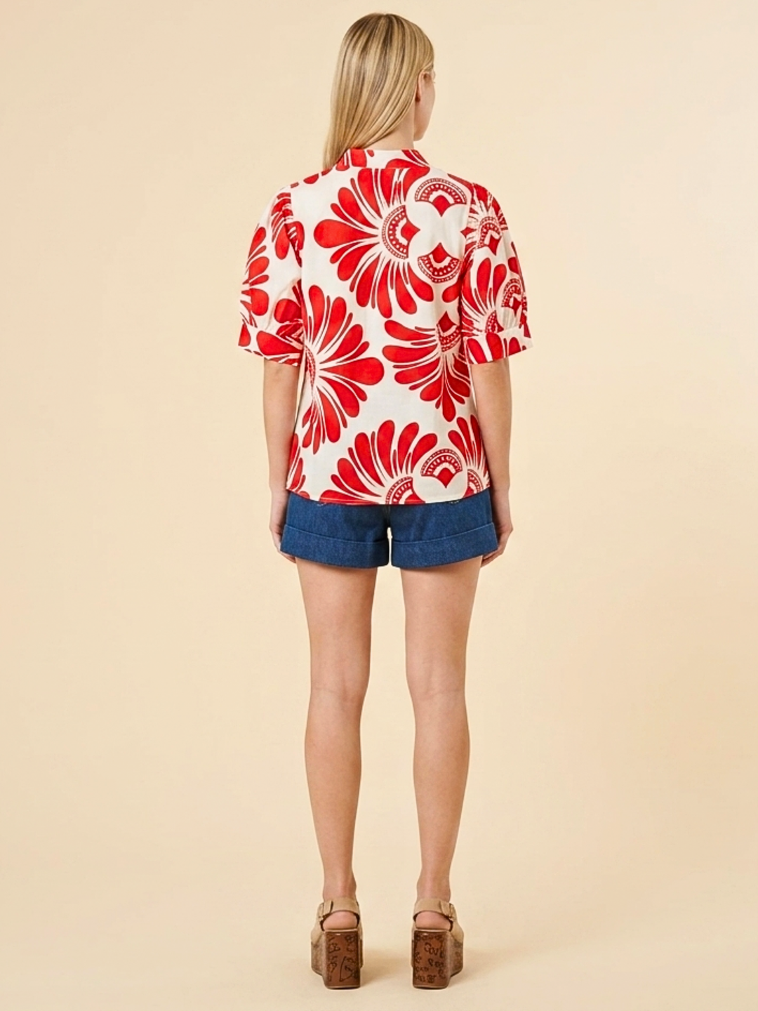 Women's short-sleeve button-up shirt in white with a bold red abstract floral print, viewed from the back.
