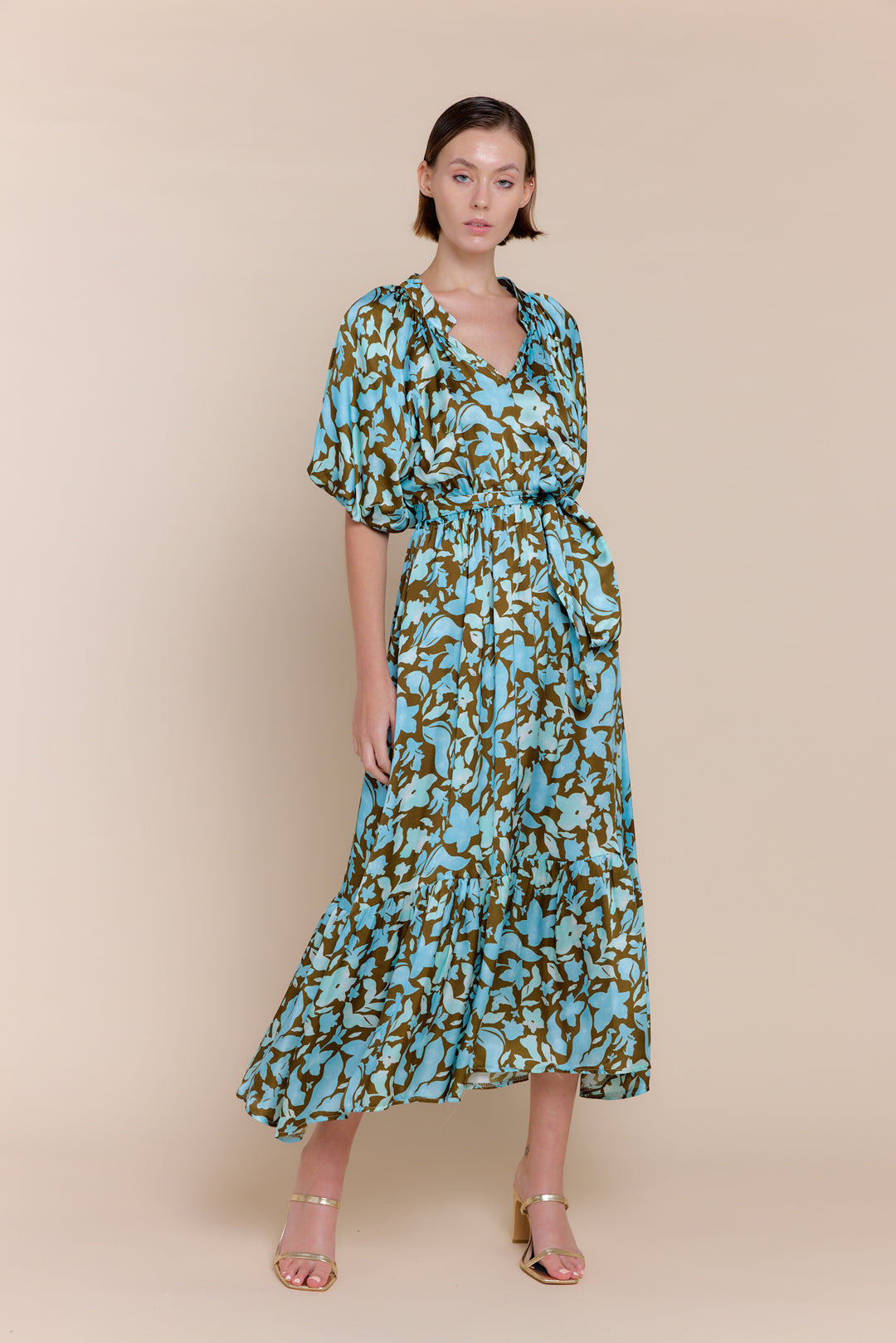 A model wearing a floral satin maxi dress with short sleeves, standing against a neutral background.
