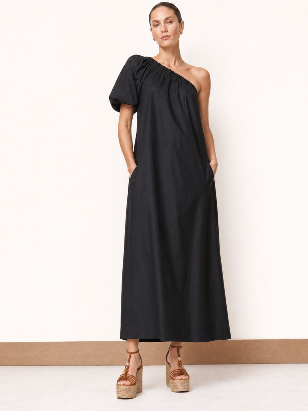 Woman wearing a black one-shoulder dress against a white background