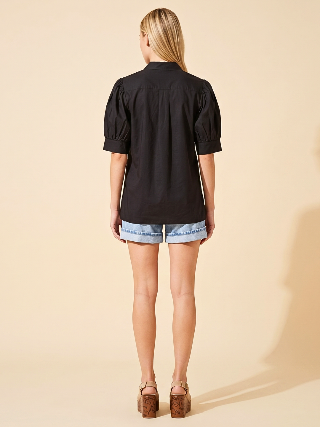 omen's black short-sleeve puff sleeve blouse with a split v-neckline and structured poplin finish, styled casually with denim shorts."