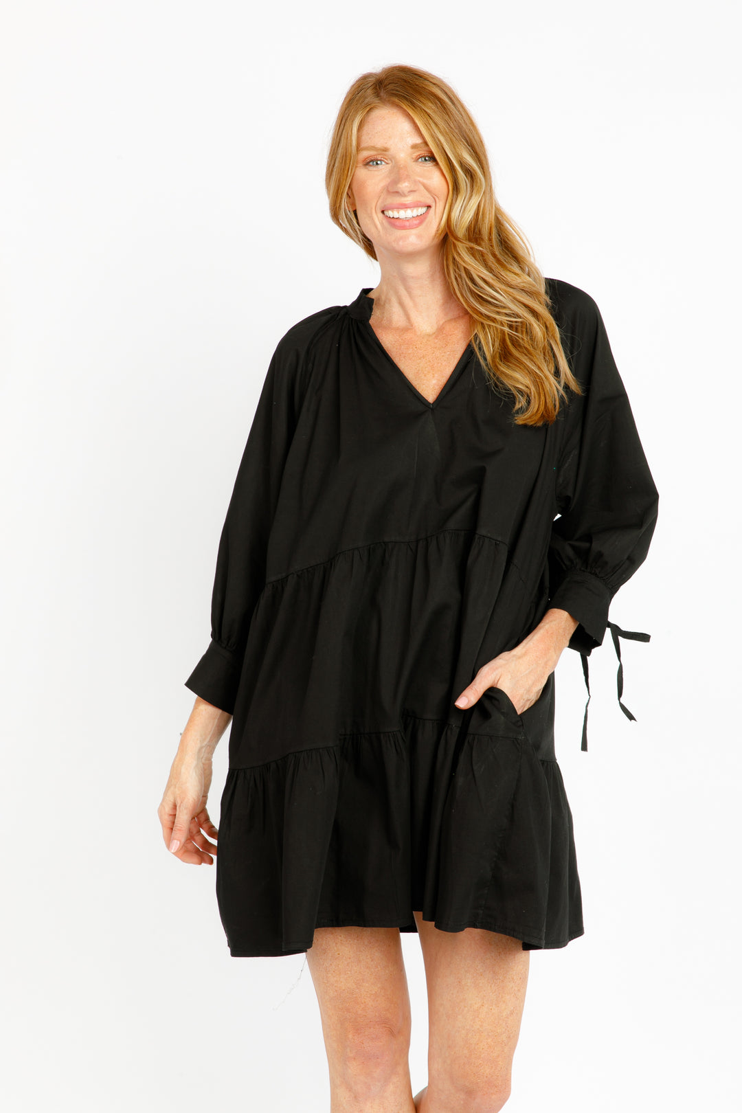 A woman modeling a green long sleeve mini dress with tie details on the sleeves.