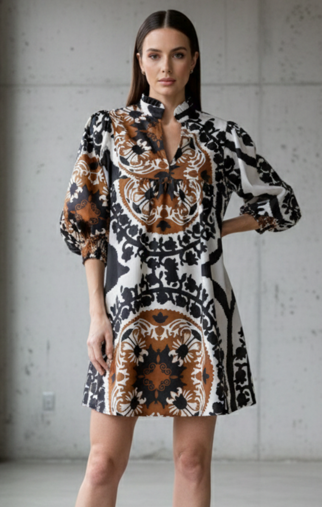 Model wearing a short, babydoll-style dress with a high mandarin collar and voluminous 3/4 sleeves. shift dress The dress features a bold, intricate medallion and scroll pattern in black, white, and rust/brown
