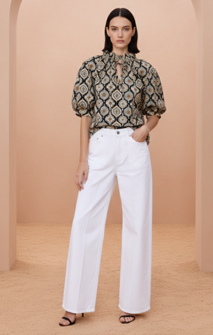 Close-up of a bohemian-style blouse featuring an intricate geometric mosaic print in black, gold, and cream. The top includes a high ruffled neckline with a delicate string tie, voluminous elbow-length puff sleeves with elastic cuffs, and a relaxed, airy fit."