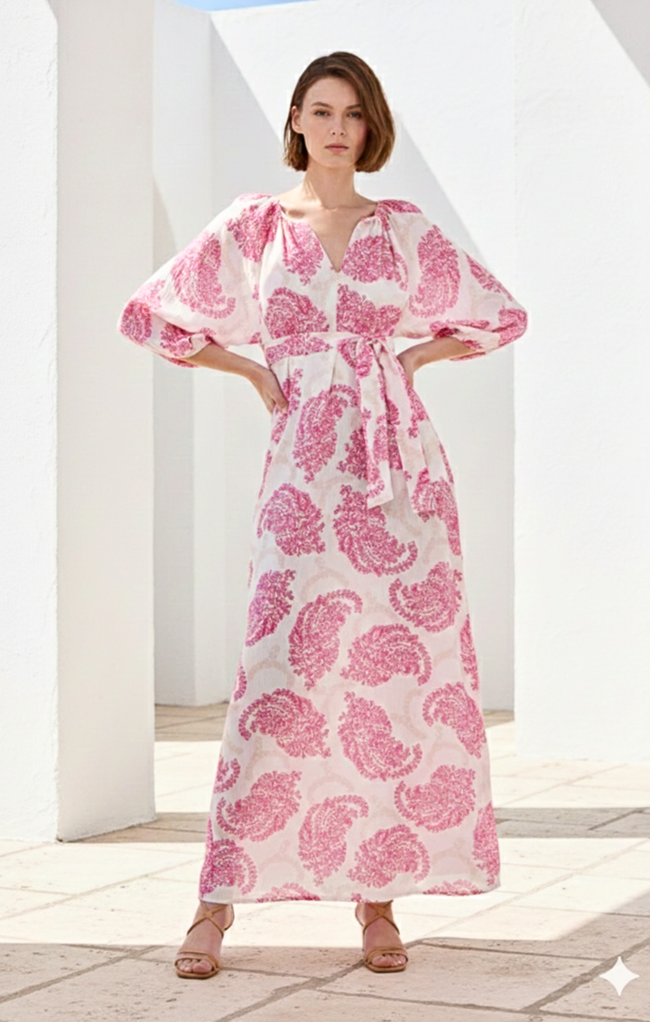 Woman wearing a pink and white patterned dress standing in a bright outdoor setting.