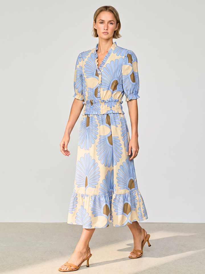 A woman modeling a light blue and cream floral print midi dress with puff sleeves and a ruffled hem, paired with tan heeled sandals against a neutral studio background.