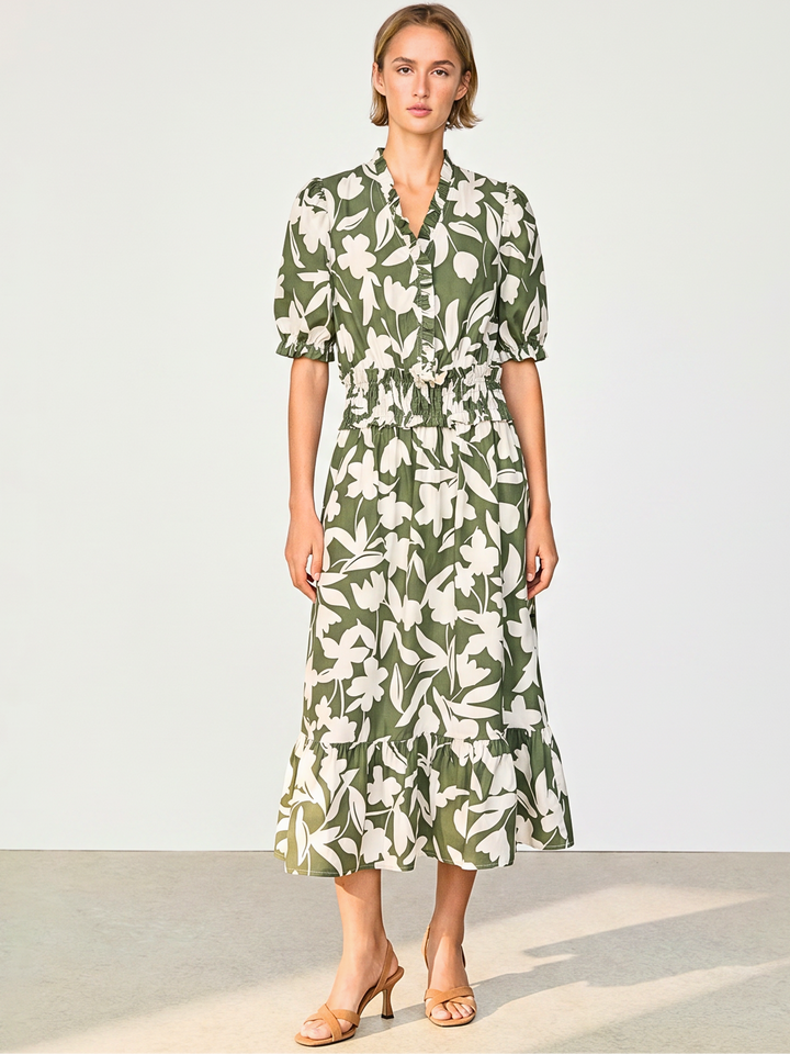 A woman modeling a green and white floral print midi dress with short puff sleeves, a button-up front, and a ruffled hem, standing against a plain light gray studio background.