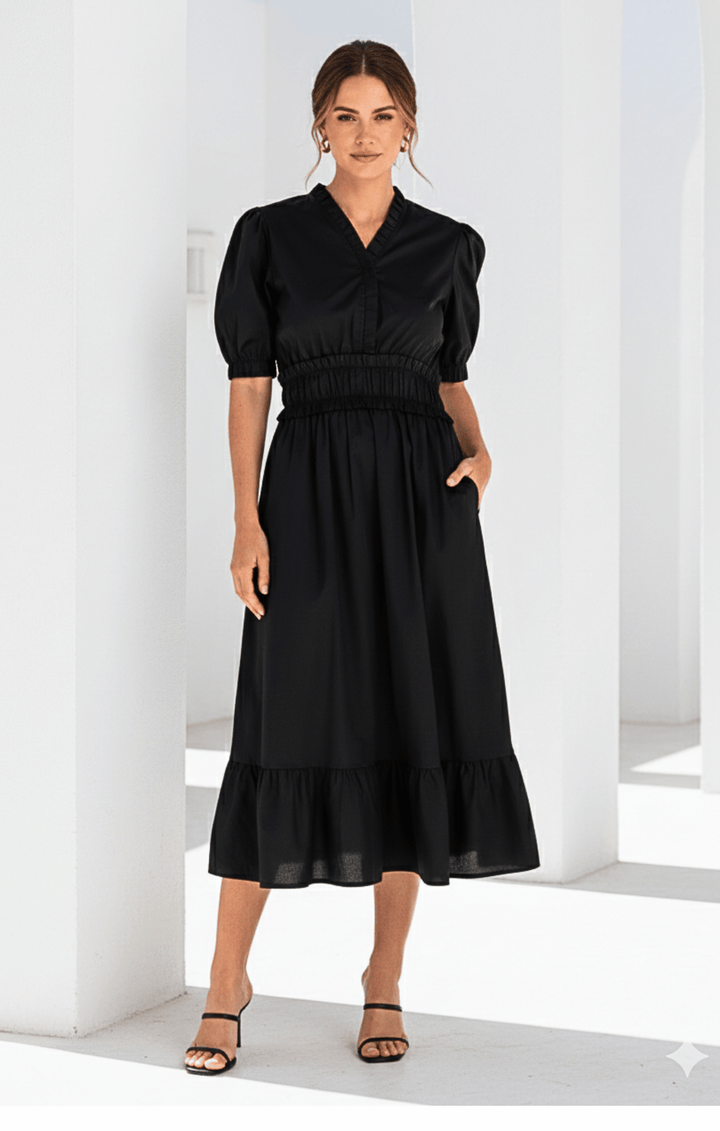 Woman wearing a black dress standing in a bright room with white walls.