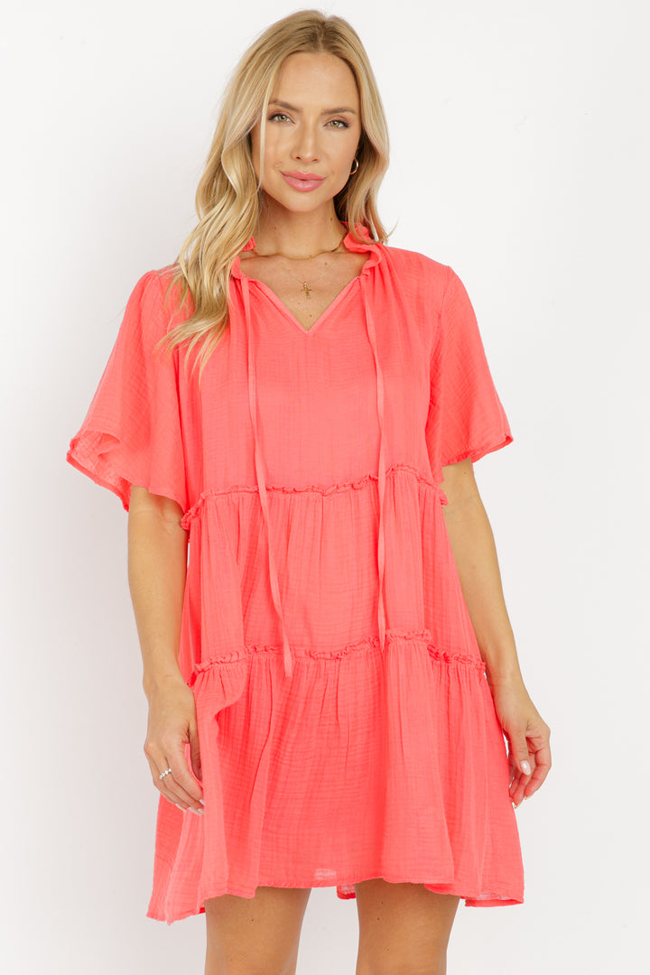 A female model wearing a red, short-sleeved, tiered tunic dress with a jersey camisole lining.