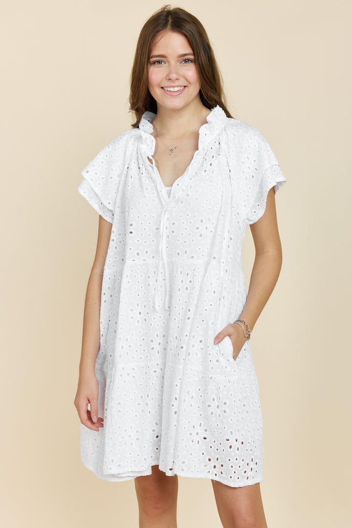 A woman wearing a white short-sleeved cotton dress with eyelet details.