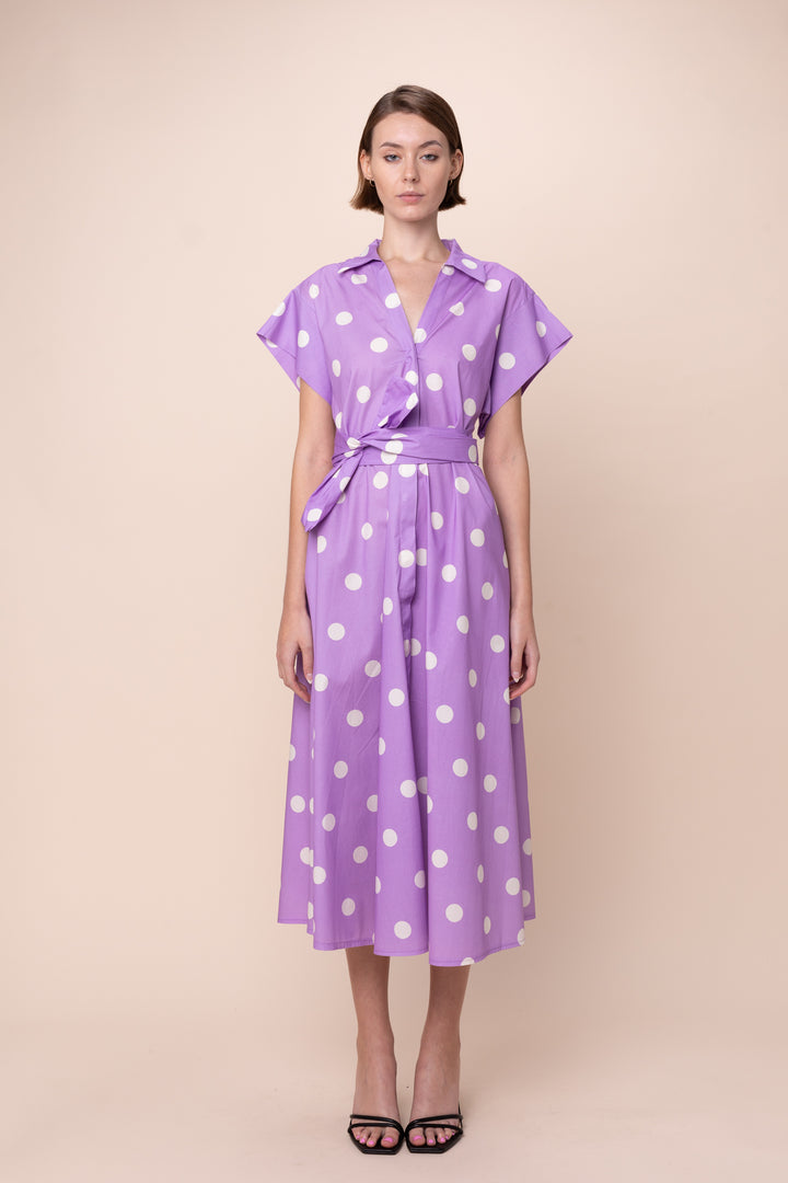 Woman wearing a purple dress with white polka dots on a beige background