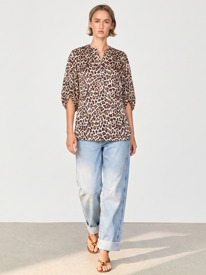 A woman modeling a leopard-print blouse with three-quarter sleeves and light-wash blue jeans, standing against a plain light gray studio background.