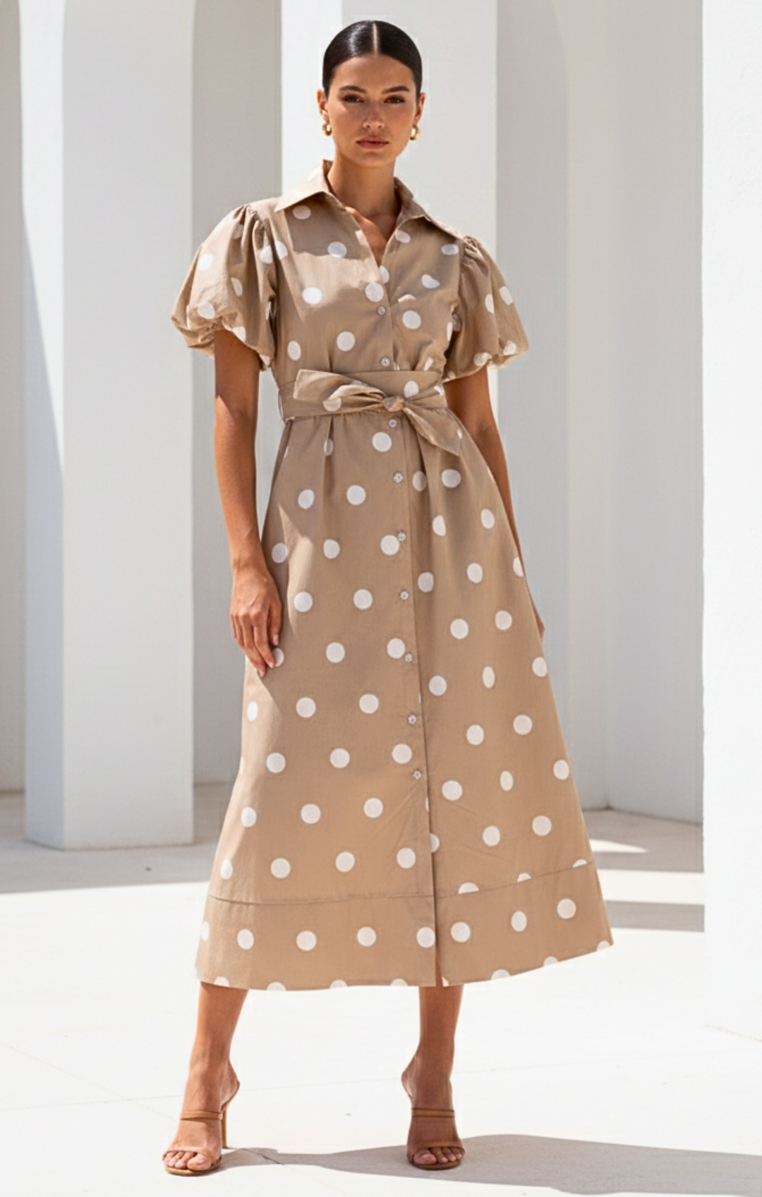Woman wearing a beige dress with white polka dots in a minimalistic setting