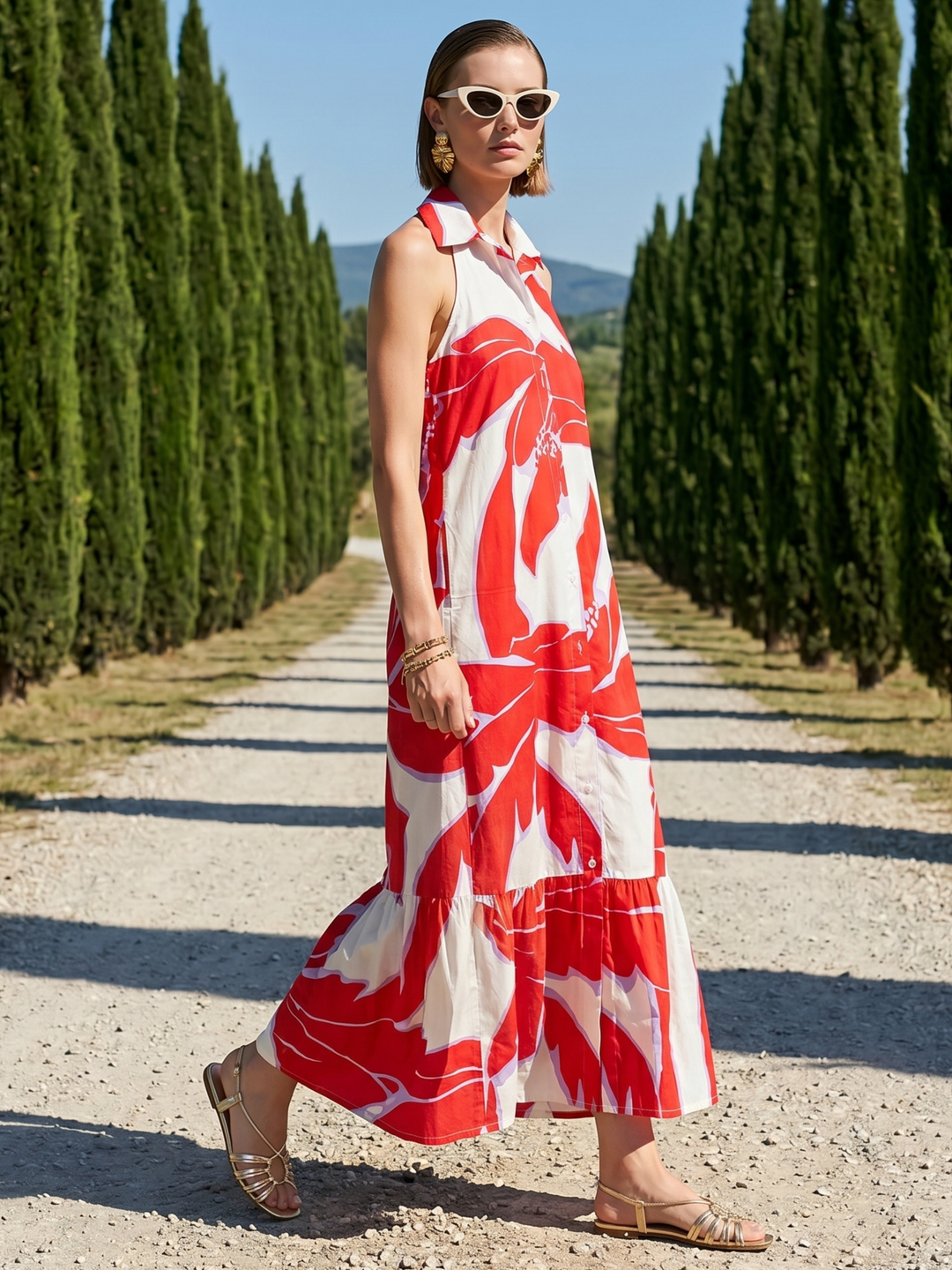 Woman in a red and white dress walking along a path lined with tall green trees.