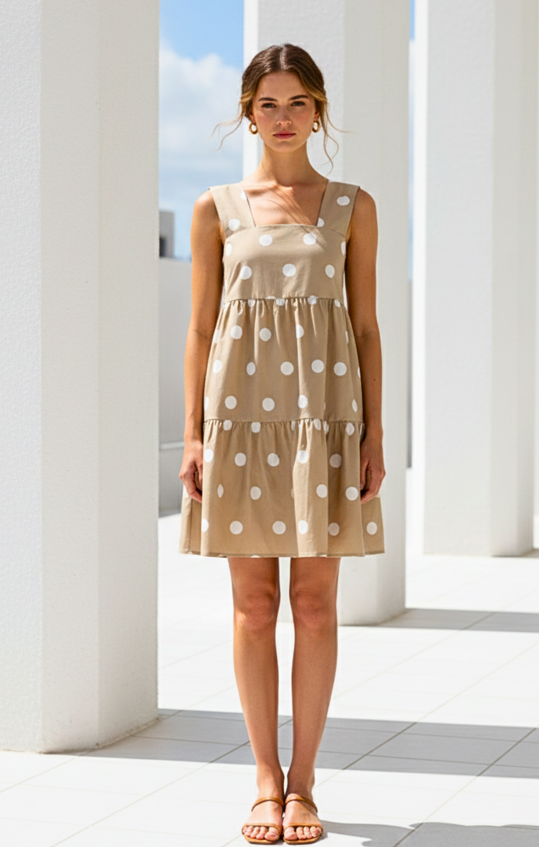 Woman wearing a beige dress with white polka dots standing in front of classical columns.
