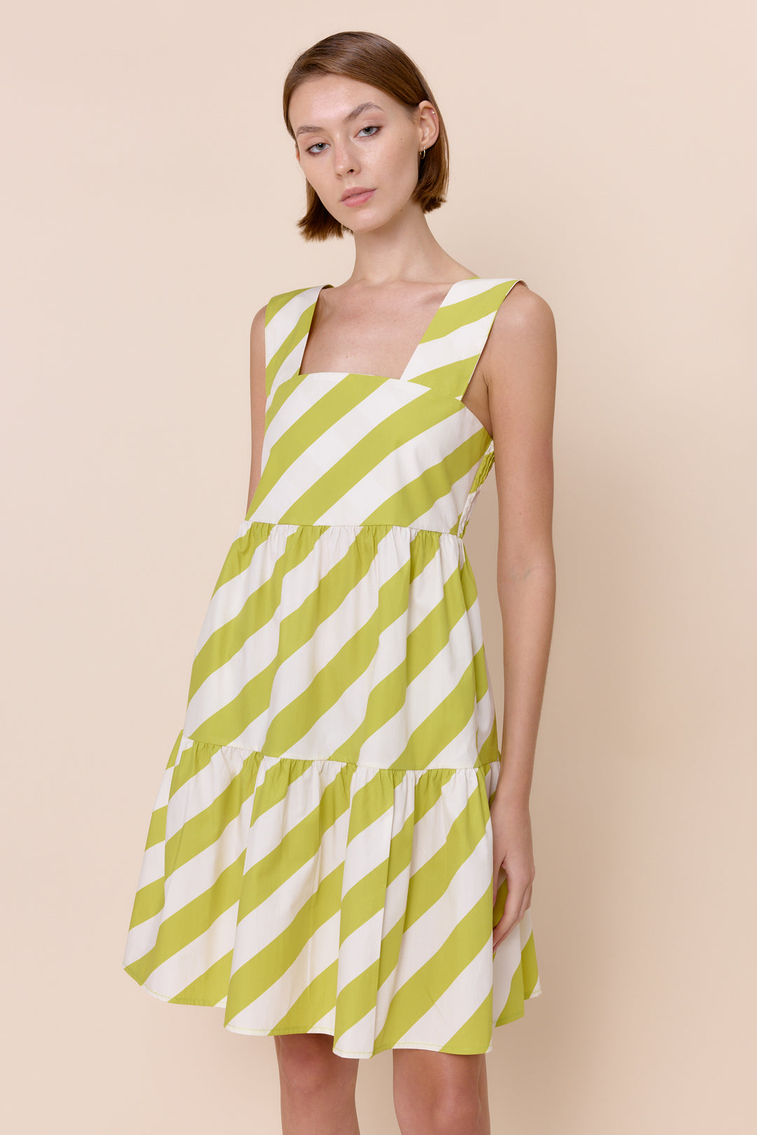 A sleeveless, mini beige and white striped dress with a square neckline and tiered skirt.