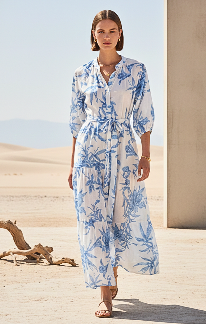 Woman wearing a blue and white floral dress standing in a desert-like setting.