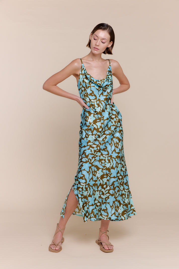 A woman wearing a blue and white floral satin dress with a cowl neckline and spaghetti straps.