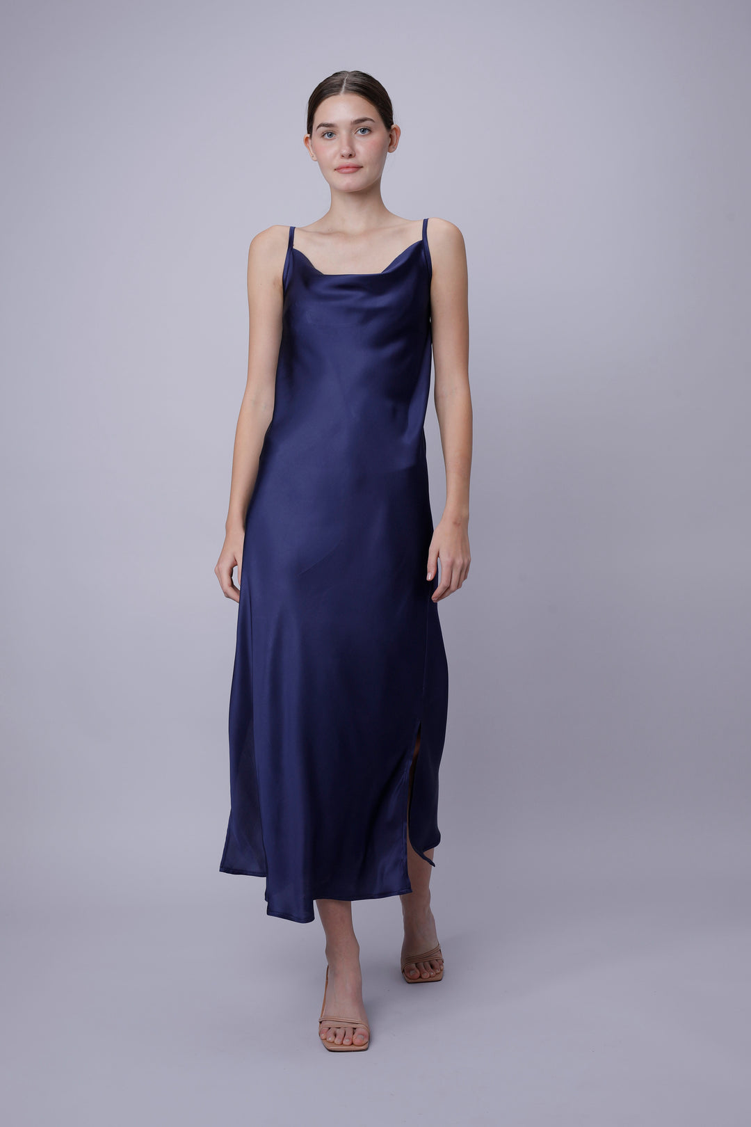 Woman wearing a navy blue satin slip dress on a light gray background