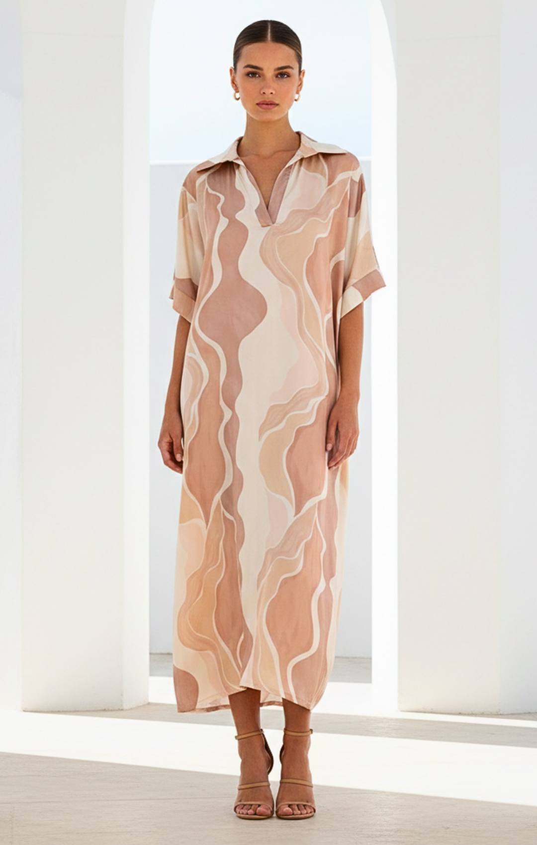 Woman wearing a patterned dress standing in a bright room with white walls.