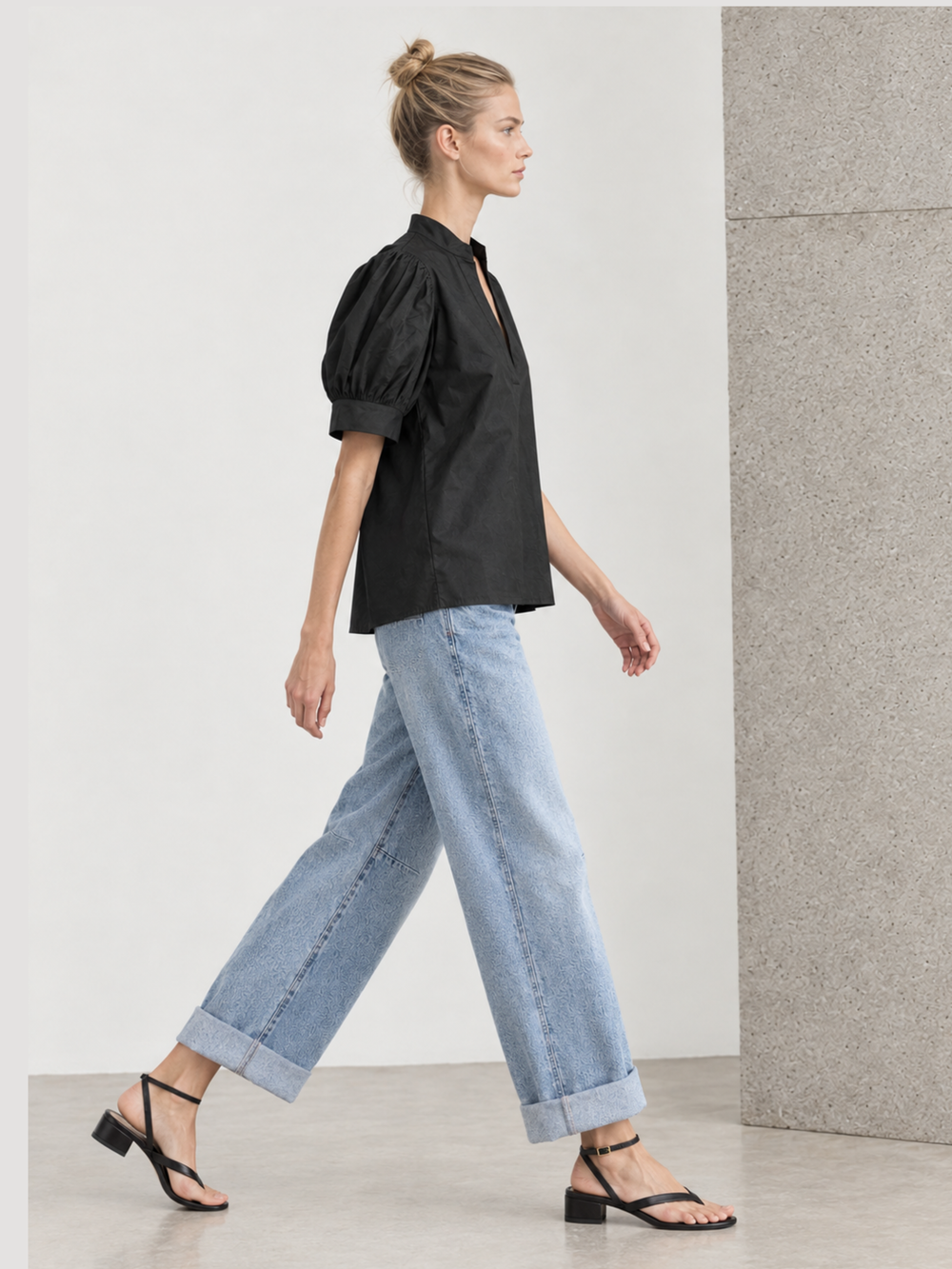 omen's black short-sleeve puff sleeve blouse with a split v-neckline and structured poplin finish, styled casually with denim shorts."