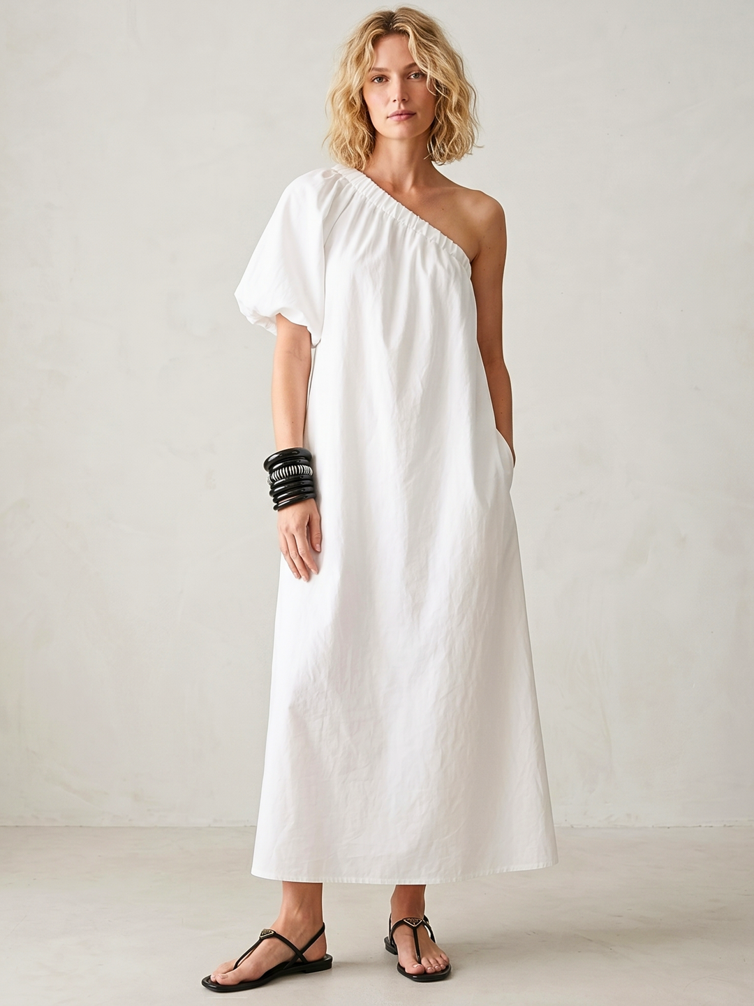 Woman wearing a white one-shoulder dress against a plain background